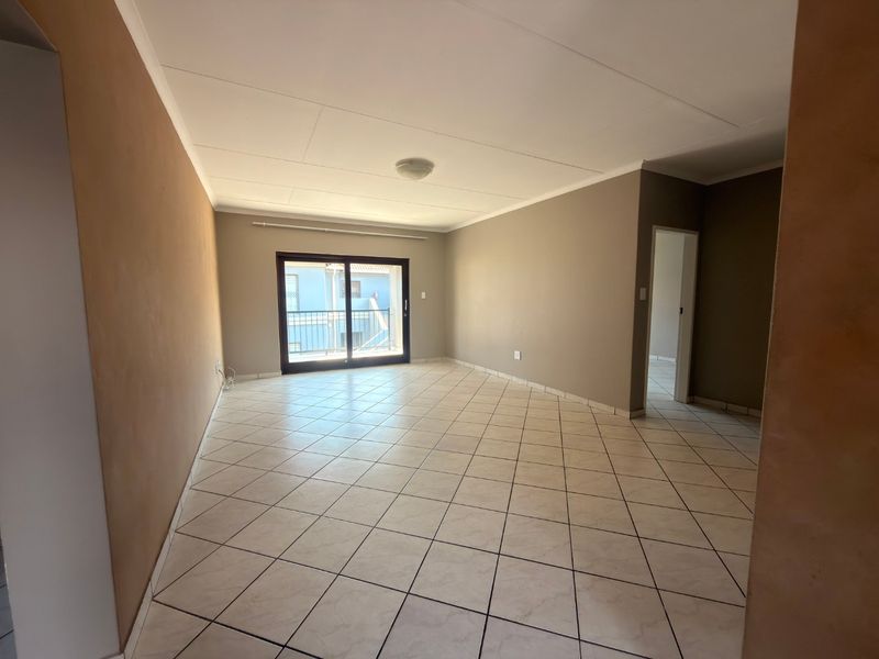 A spacious, empty living area featuring neutral-toned walls, tiled flooring, and a sliding glass door providing access to an outdoor balcony.