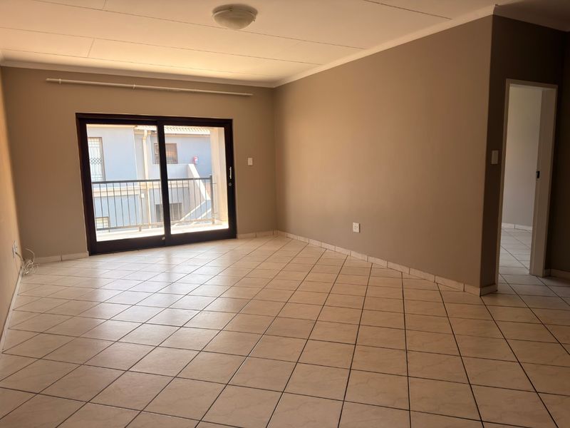 A spacious, empty living room featuring neutral wall tones, tiled flooring, and a sliding glass door providing access to a balcony.