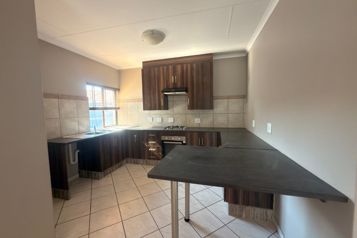 A functional kitchen featuring dark wood-look cabinetry, laminate countertops, a gas hob with extractor, and neutral tiled flooring and backsplash.
