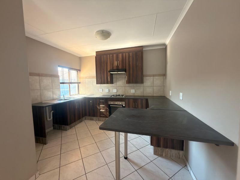A functional kitchen featuring dark wood-look cabinetry, laminate countertops, a gas hob with extractor, and neutral tiled flooring and backsplash.