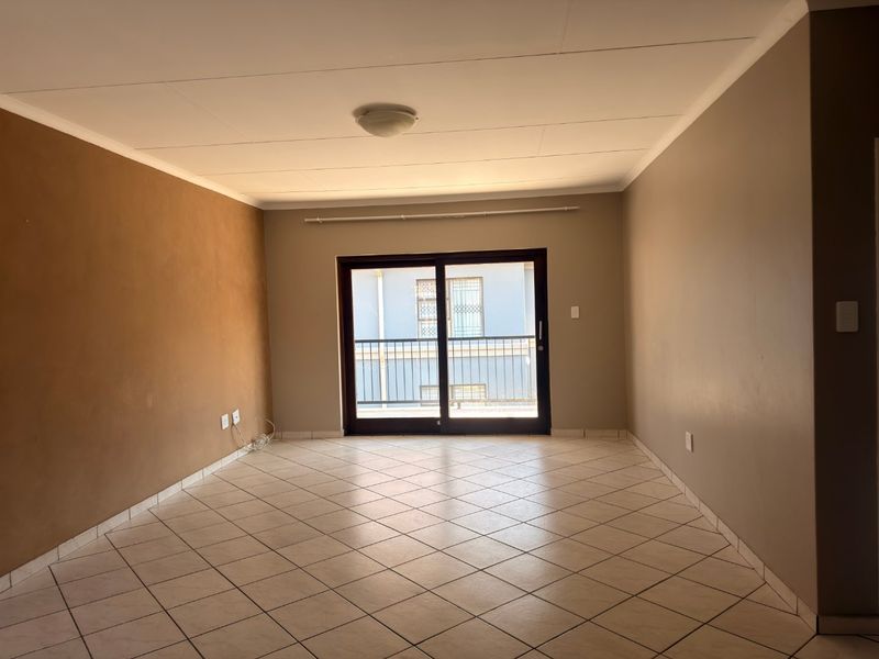 An empty living room featuring tiled flooring, neutral wall tones, and a sliding glass door providing access to an outdoor balcony area.