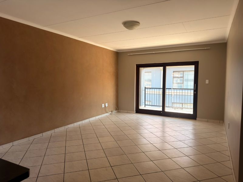 An empty living room featuring tiled flooring and a sliding glass door providing access to a balcony.