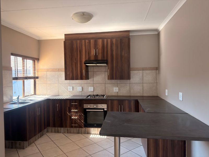A clean, functional kitchen featuring dark wood-grain cabinetry, dark laminate countertops, a gas hob, built-in oven, and neutral tiled backsplash and flooring.