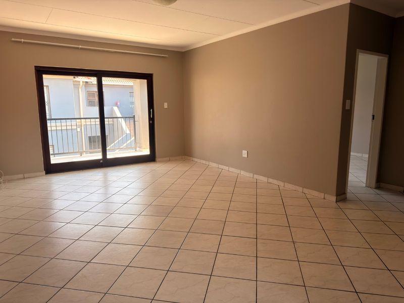 A spacious, empty living area featuring neutral wall tones, tiled flooring, and a sliding glass door providing access to an outdoor balcony.