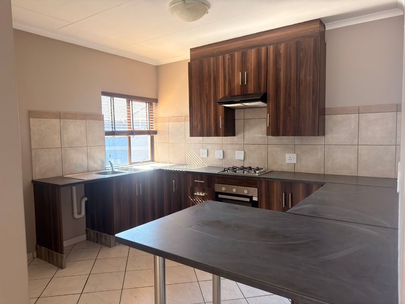 A functional kitchen featuring dark wood-look cabinetry, dark countertops, a gas hob, built-in oven, and neutral tiled backsplash and flooring.