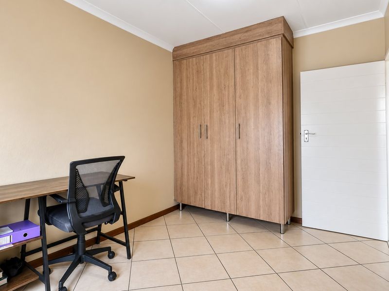 A bedroom featuring neutral wall tones, tiled flooring, and a large built-in wooden wardrobe with modern finishes.