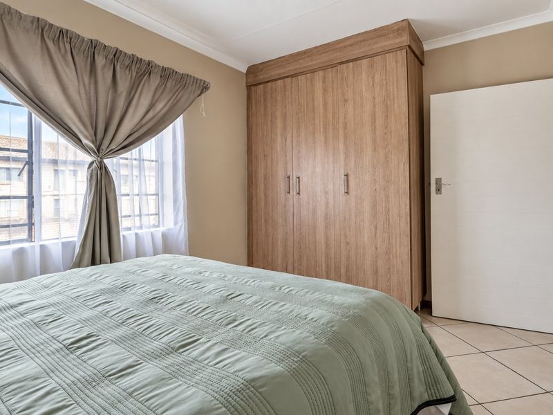 A well-maintained bedroom featuring tiled flooring, a large built-in wooden wardrobe, and a window fitted with security bars.