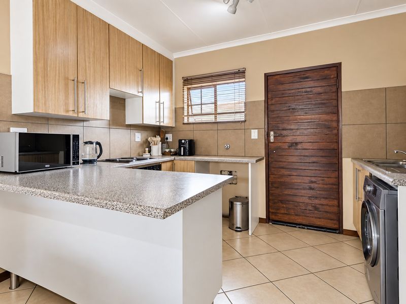 A functional kitchen featuring light wood cabinetry, granite countertops, tiled backsplash, and dedicated plumbing for a washing machine.