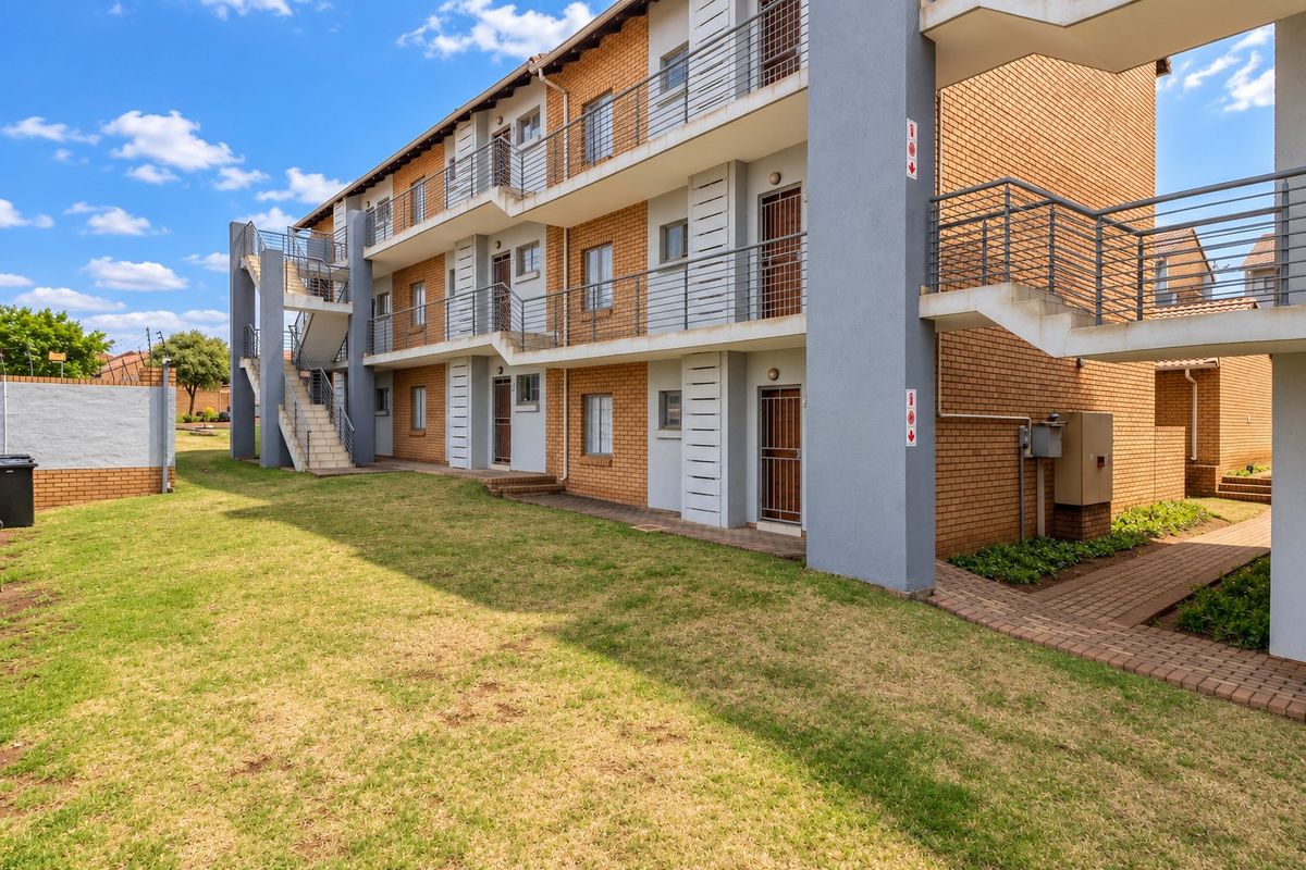 Rear view of a multi-story apartment complex featuring brick facade, external concrete staircases, and metal security railings.