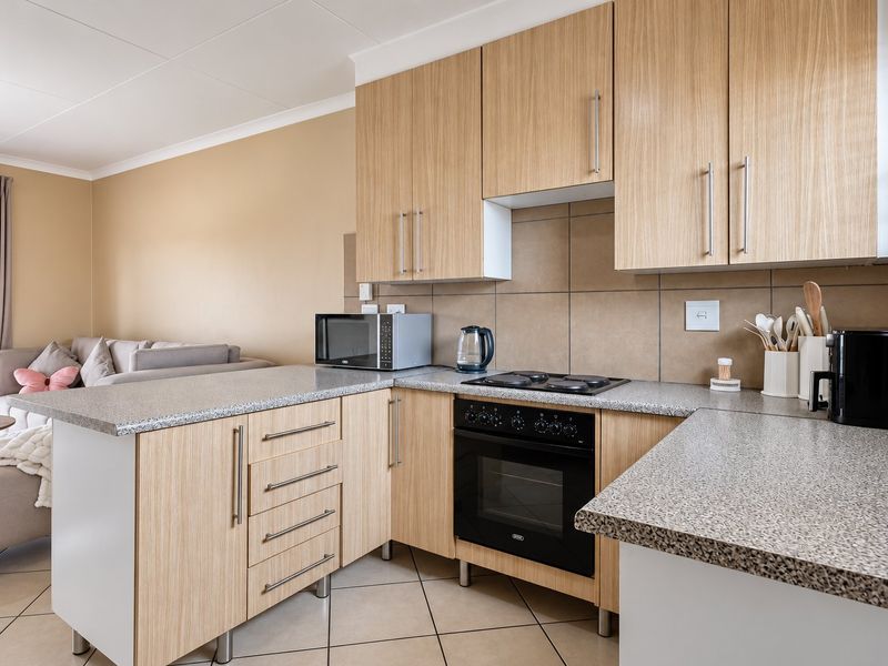 Open-plan kitchen featuring light wood-finish cabinetry, granite-look countertops, built-in oven, and electric hob, seamlessly flowing into the adjacent living area.