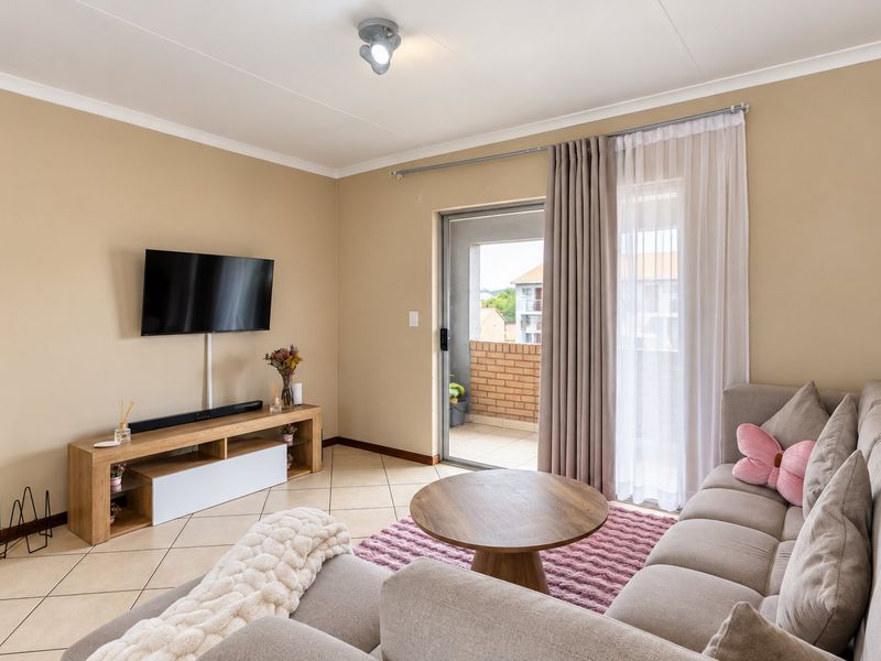 A well-maintained living room featuring tiled flooring, neutral wall tones, and a sliding glass door providing access to an outdoor balcony.