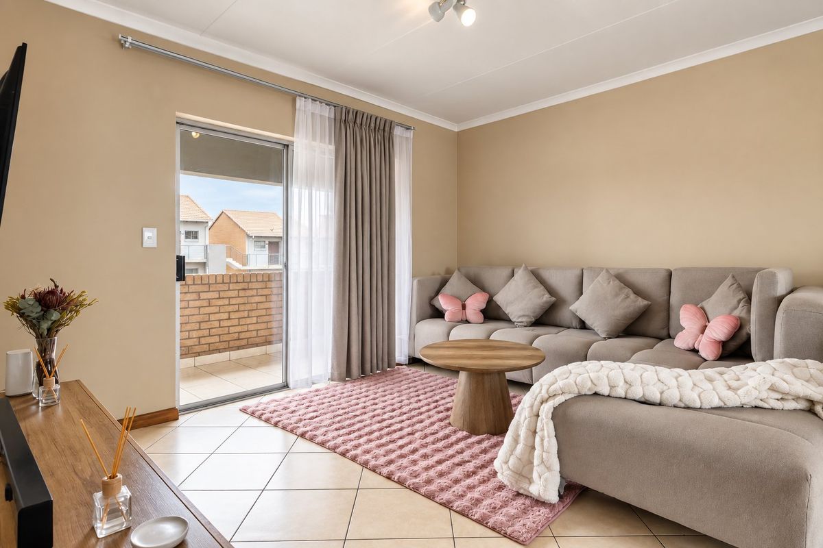 A well-maintained living room featuring ceramic floor tiles, neutral wall tones, and a sliding glass door providing access to an outdoor balcony area.