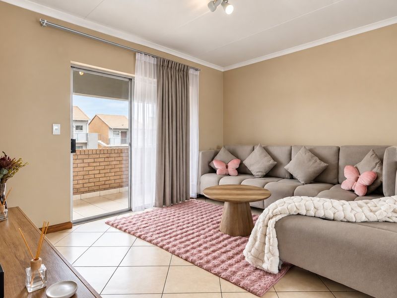 A well-maintained living room featuring ceramic floor tiles, neutral wall tones, and a sliding glass door providing access to an outdoor balcony area.