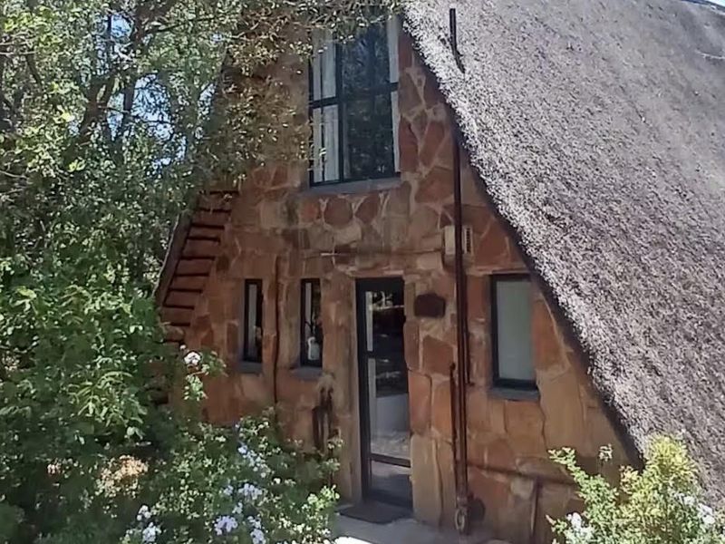 A charming A-frame cottage featuring traditional thatch roofing and rustic stone exterior cladding, set within a landscaped garden.
