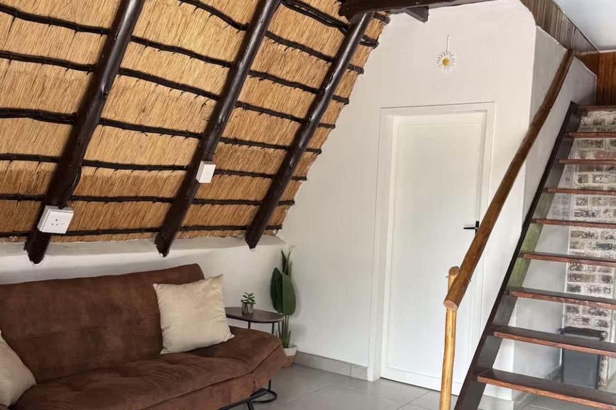 Living area featuring a unique thatched roof with exposed timber rafters, tiled flooring, and a wooden staircase leading to an upper level.