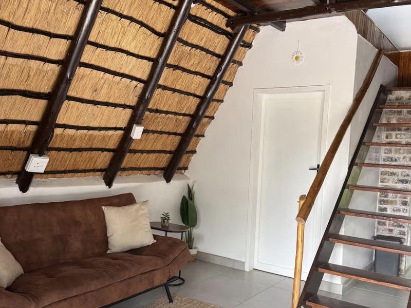 Living area featuring a unique thatched roof with exposed timber rafters, tiled flooring, and a wooden staircase leading to an upper level.
