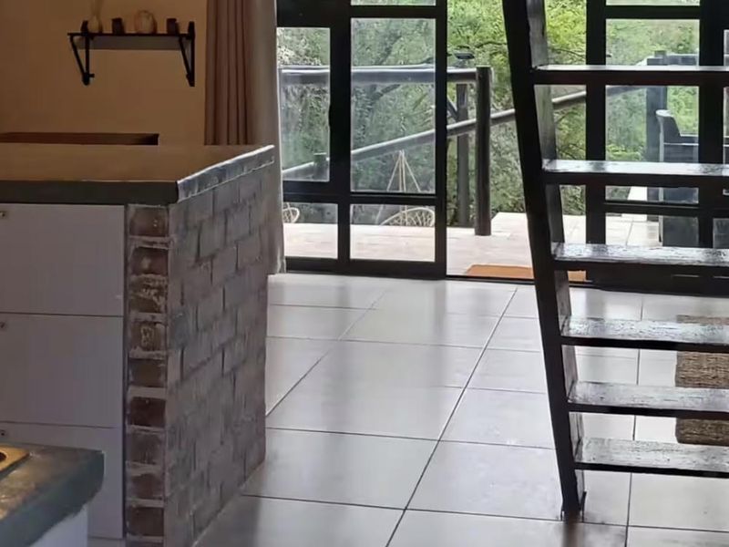 Open plan living area featuring tiled floors, an exposed brick kitchen island, and large black-framed glass doors leading to an outdoor space.