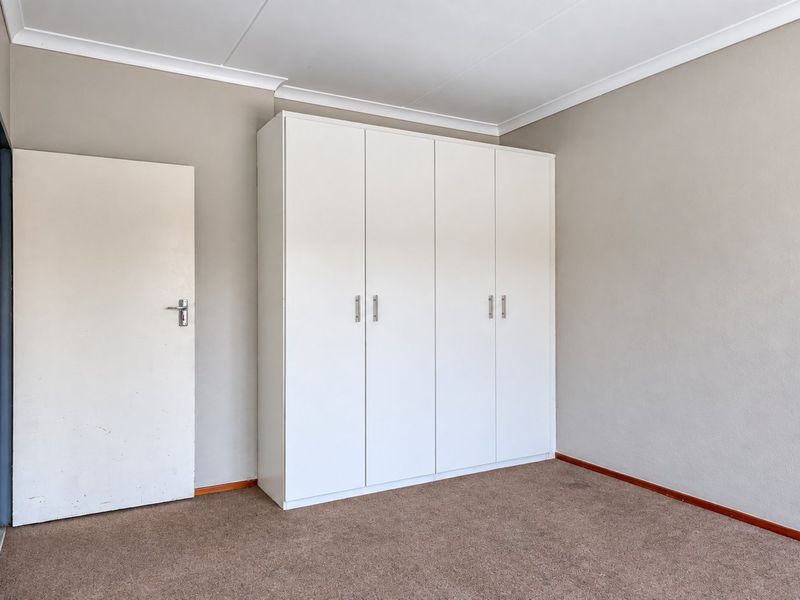 A clean, empty bedroom featuring neutral wall paint, carpeted flooring, and a white built-in wardrobe with ample storage space.
