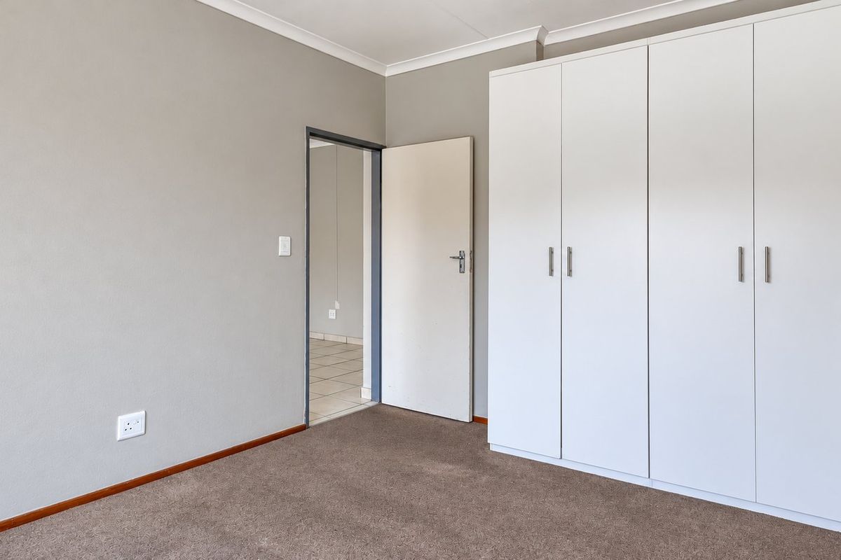 A clean, empty bedroom featuring neutral wall paint, carpeted flooring, and ample built-in cupboard storage space.