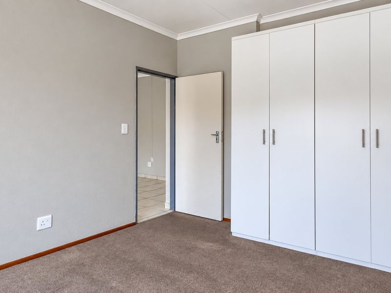 A clean, empty bedroom featuring neutral wall paint, carpeted flooring, and ample built-in cupboard storage space.