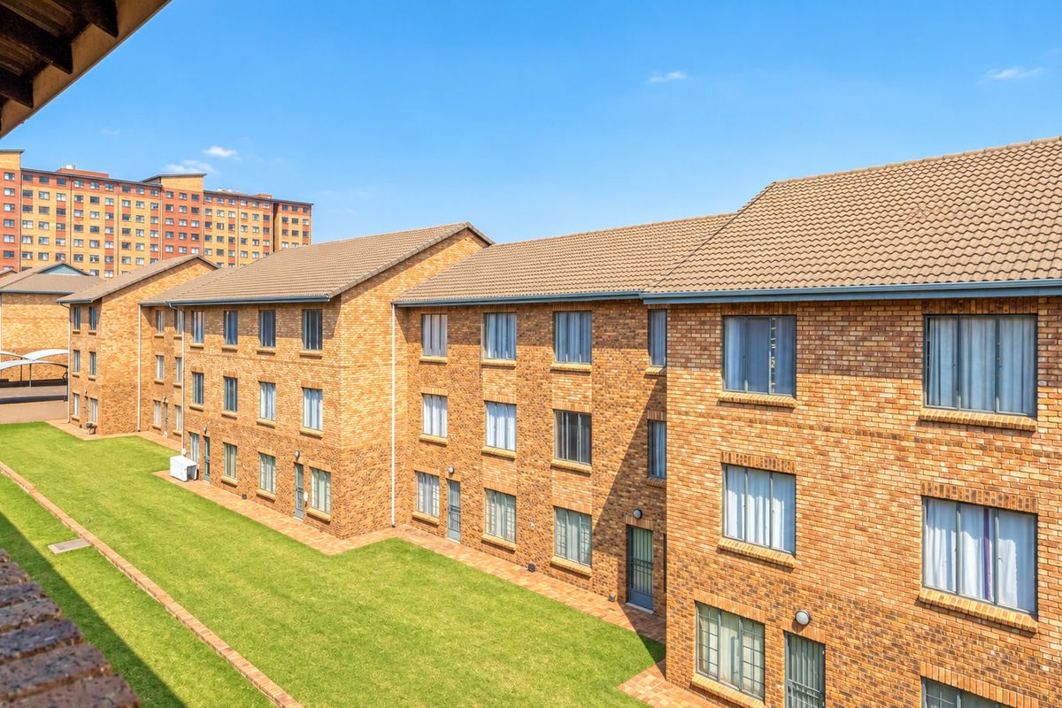 Exterior view of a multi-story apartment complex featuring face brick facades, tiled roofing, and well-maintained communal lawn areas.