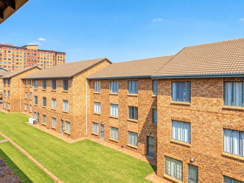 Exterior view of a multi-story apartment complex featuring face brick facades, tiled roofing, and well-maintained communal lawn areas.