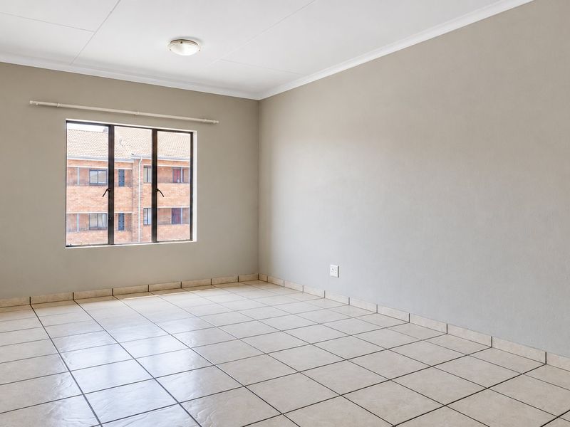 A bright, empty bedroom featuring neutral wall paint, tiled flooring, and a large window providing natural light.