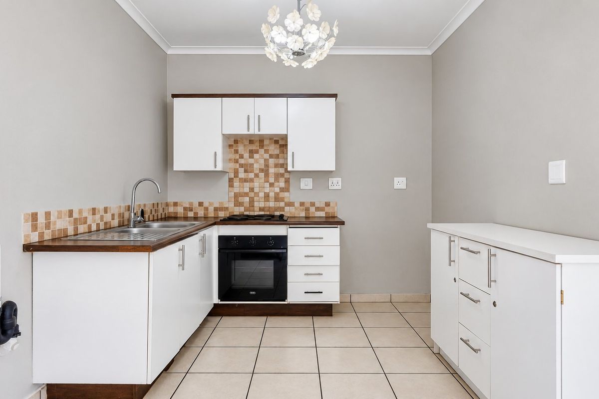 A clean, functional kitchen featuring white cabinetry, dark laminate countertops, a built-in oven with gas hob, and neutral tiled flooring.