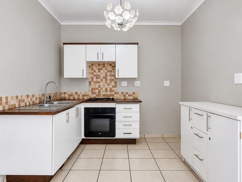 A clean, functional kitchen featuring white cabinetry, dark laminate countertops, a built-in oven with gas hob, and neutral tiled flooring.