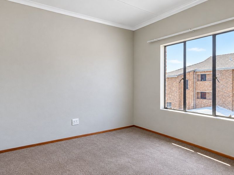 A bright, empty bedroom featuring neutral walls, carpeted flooring, and a built-in wardrobe, offering a clean canvas for personalization.