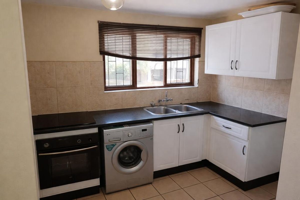 A functional kitchen featuring built-in cabinetry, a double sink, electric oven and hob, tiled backsplash, and tiled flooring.