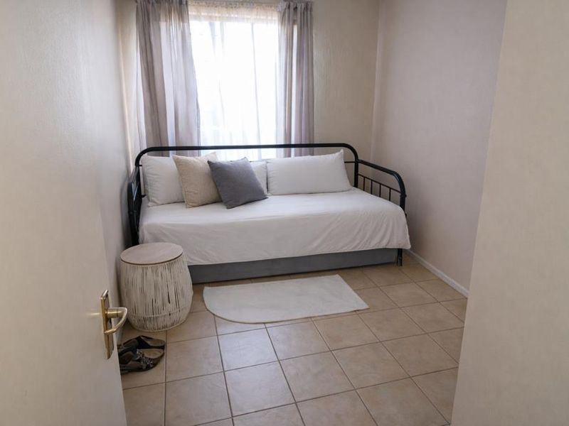A compact bedroom featuring neutral tiled flooring and a window with installed curtain tracks, offering a simple and functional living space.
