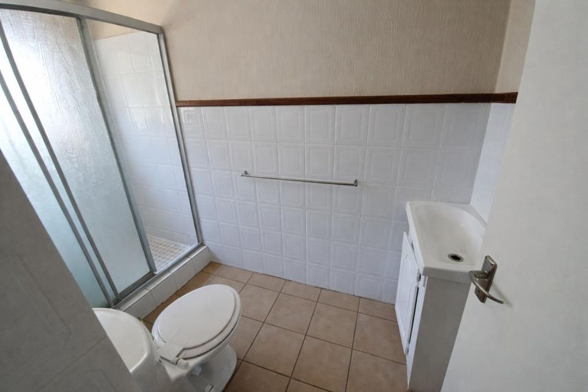 A functional bathroom featuring a shower enclosure, toilet, and vanity basin with tiled finishes throughout.