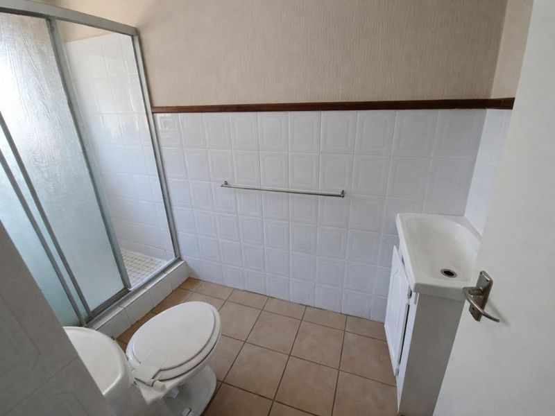 A functional bathroom featuring a shower enclosure, toilet, and vanity basin with tiled finishes throughout.