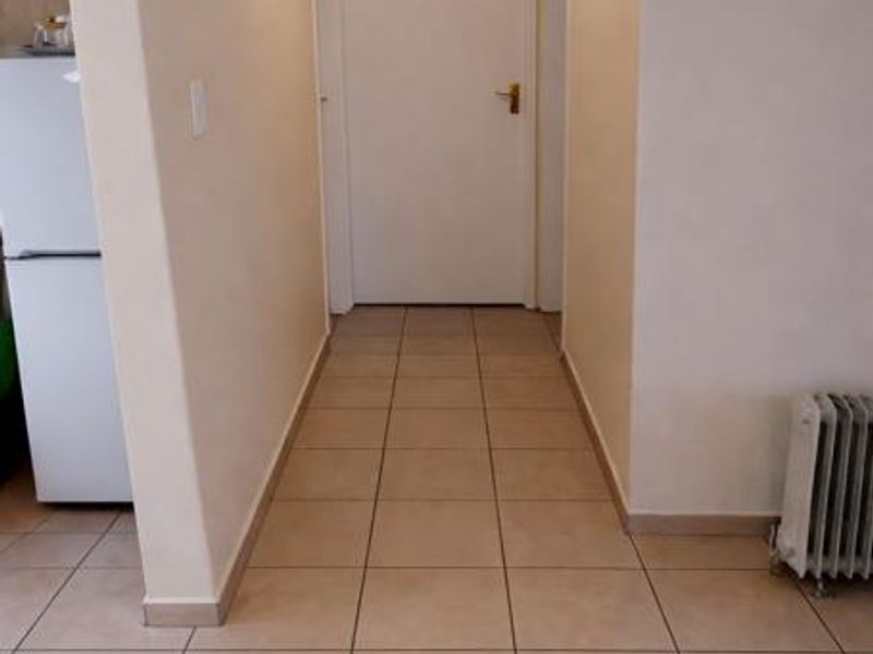 A clean, tiled hallway featuring neutral walls, a central ceiling light, and access to adjacent rooms.