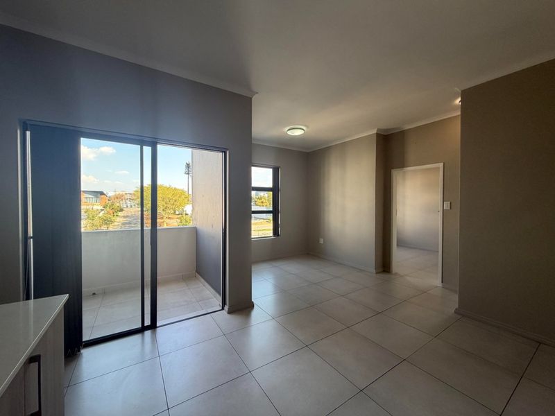 An open-plan living area featuring neutral tiled flooring, clean wall finishes, and direct access to a private balcony through a sliding glass door.