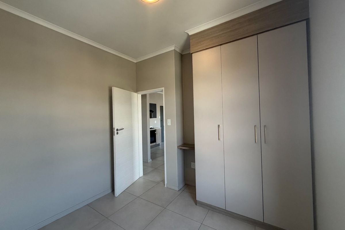 A clean, modern bedroom featuring neutral wall tones, large built-in cupboards, and tiled flooring, offering a bright and versatile living space.