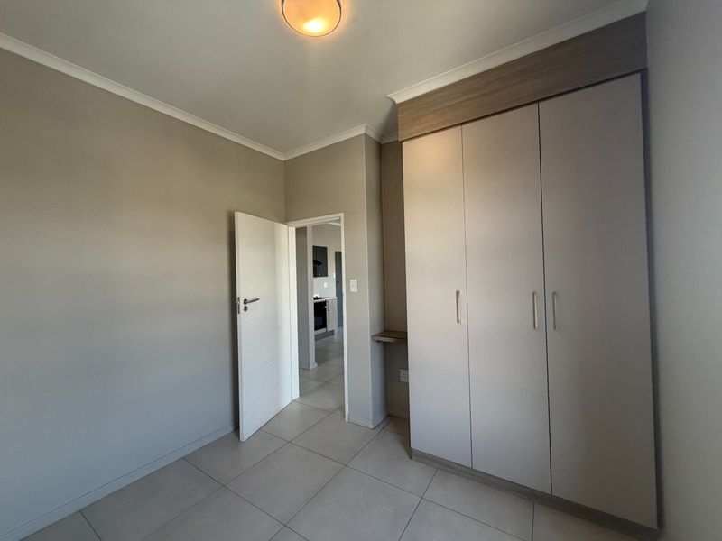 A clean, modern bedroom featuring neutral wall tones, large built-in cupboards, and tiled flooring, offering a bright and versatile living space.