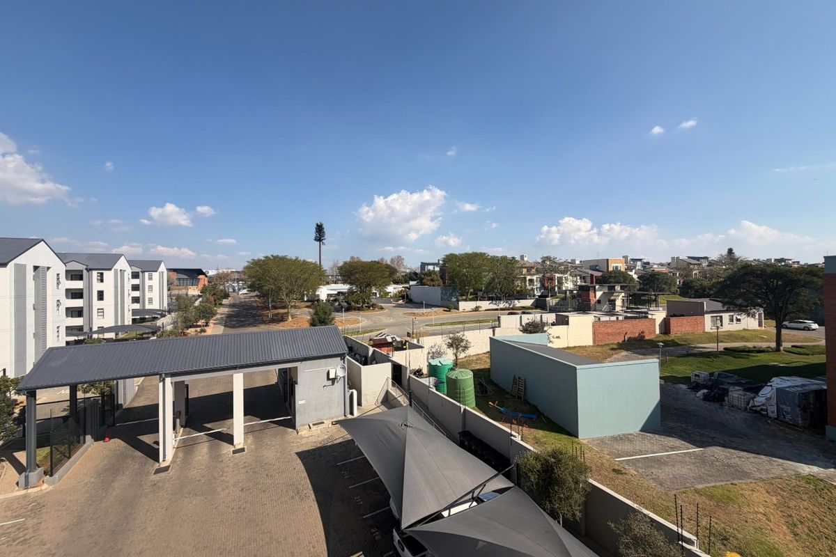 An elevated aerial view of the apartment complex grounds, featuring a paved driveway, security entrance, and covered parking bays.