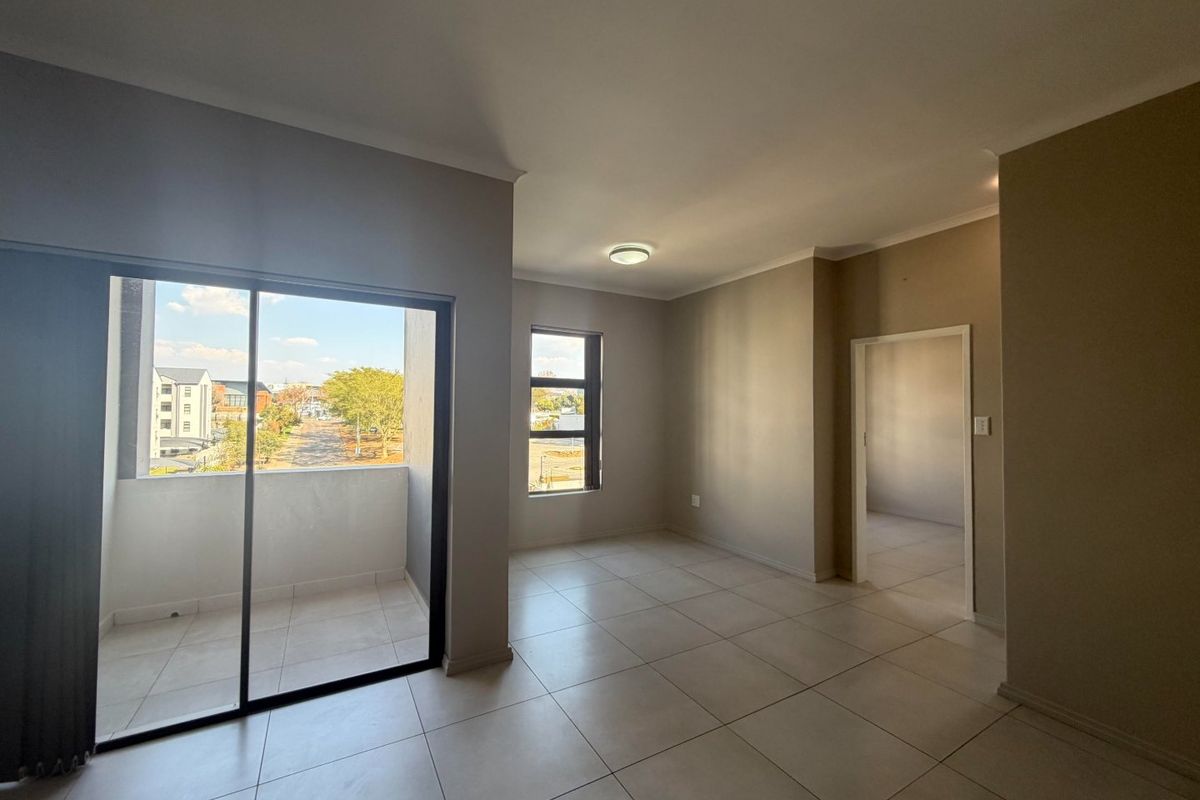 An empty, well-lit living area featuring neutral tiled flooring, a sliding door leading to a balcony, and clean, modern finishes.