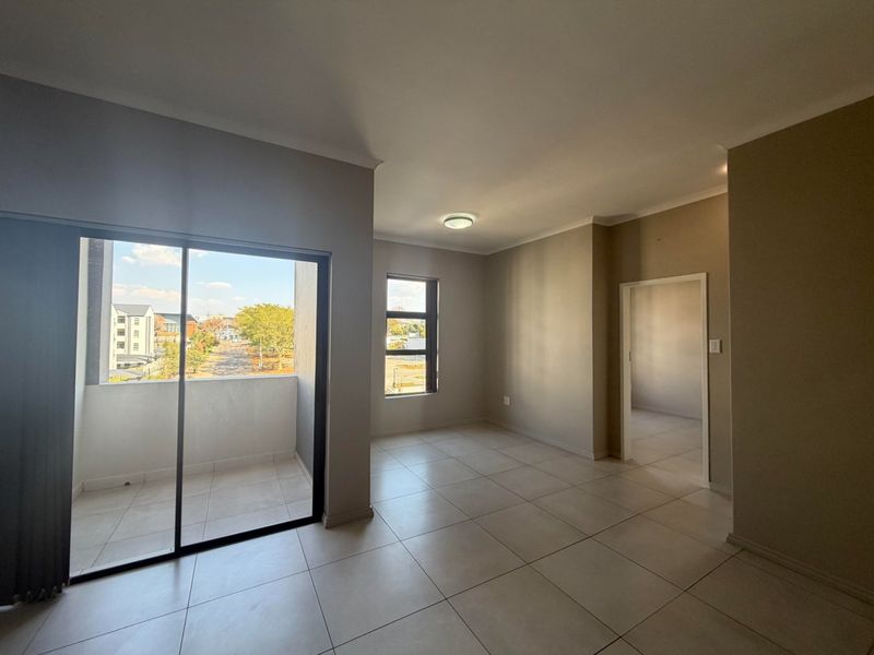 An empty, well-lit living area featuring neutral tiled flooring, a sliding door leading to a balcony, and clean, modern finishes.