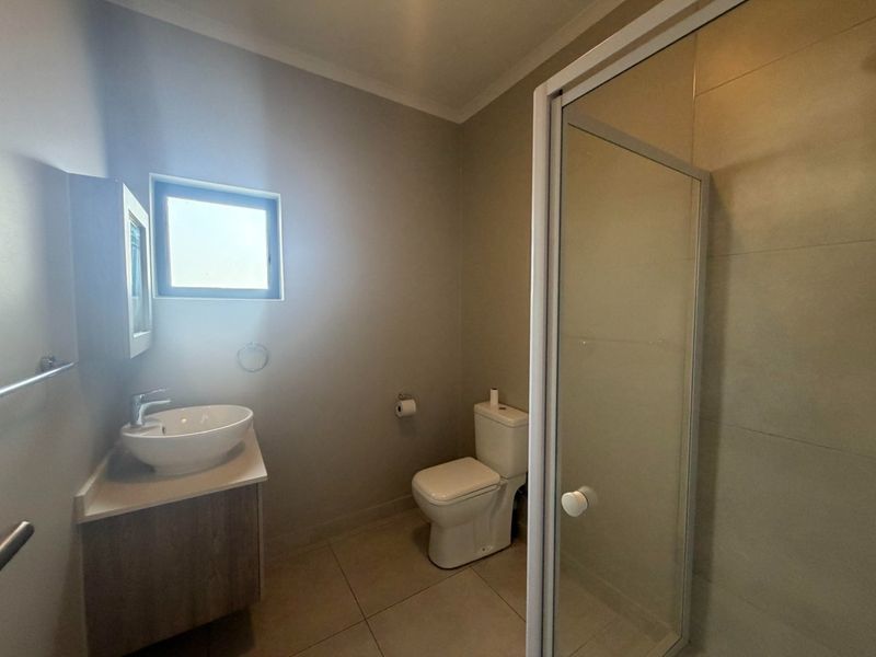 A clean and modern bathroom featuring a vanity with a vessel sink, a toilet, and a glass-enclosed shower with tiled finishes.