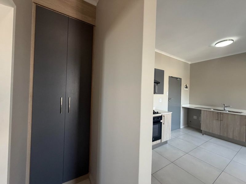 Modern kitchen featuring built-in cabinetry, integrated oven and hob, stainless steel sink, and neutral tiled flooring in an open-plan layout.
