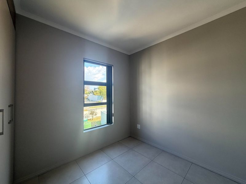 A clean, empty bedroom featuring neutral wall paint, tiled flooring, and built-in cupboards, offering a bright and versatile space.