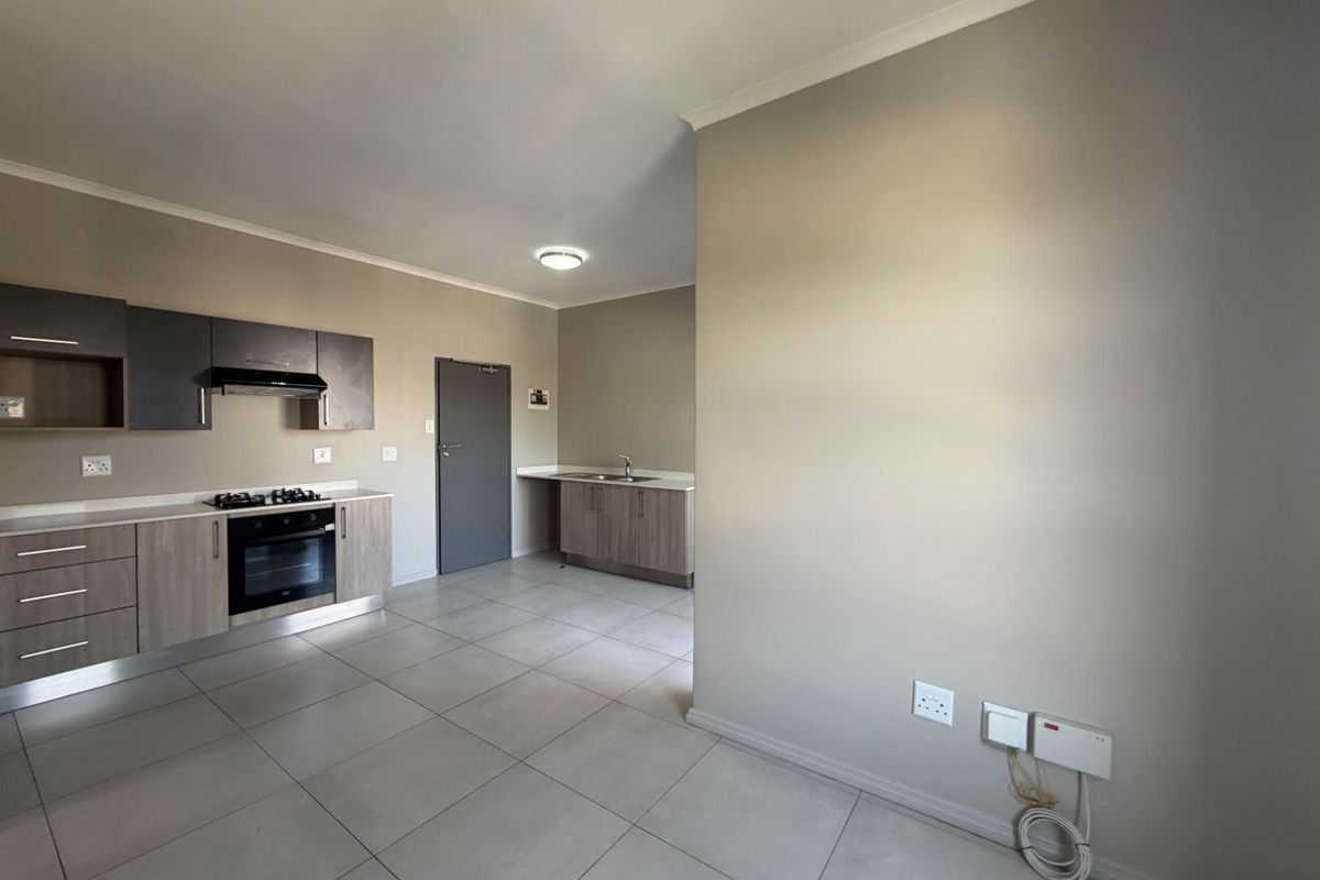 Modern open-plan kitchen featuring built-in cabinetry, gas hob, electric oven, extractor fan, and stainless steel sink with neutral tiled flooring.