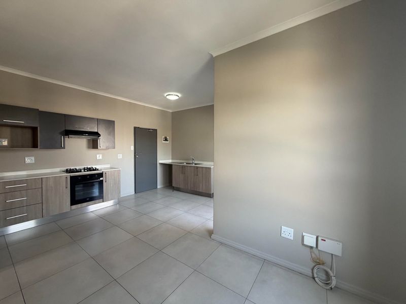Modern open-plan kitchen featuring built-in cabinetry, gas hob, electric oven, extractor fan, and stainless steel sink with neutral tiled flooring.