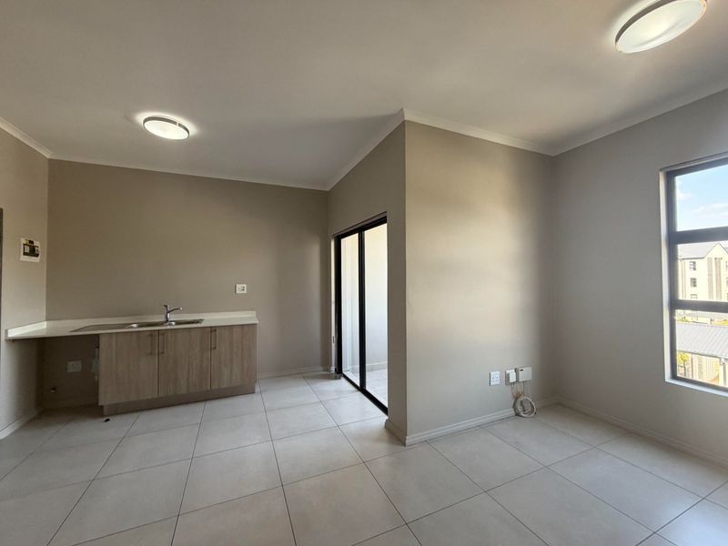 An open-plan living area featuring tiled flooring, a compact kitchen unit with a sink, and a sliding door leading to an outdoor space.