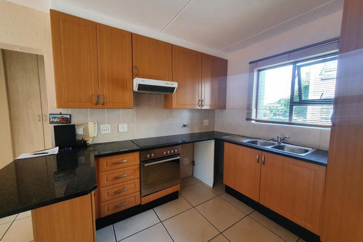 A functional kitchen featuring wood-finish cabinetry, granite countertops, a built-in oven with extractor fan, and a double basin sink with tiled flooring.