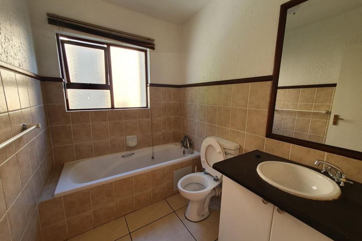 A functional bathroom featuring a bathtub, toilet, and vanity cabinet with a basin, finished with neutral wall and floor tiles.