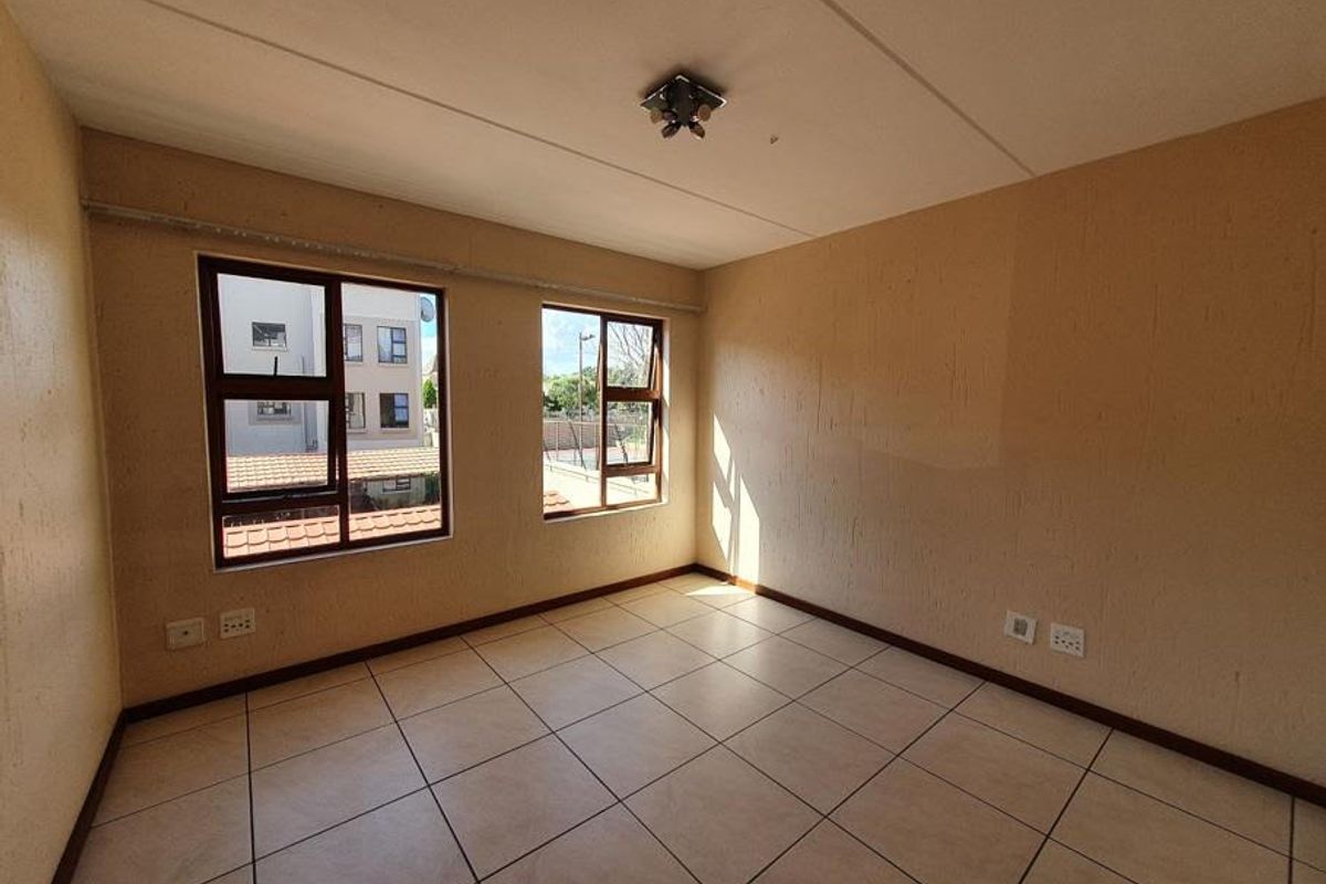 An empty bedroom featuring neutral textured walls, tiled flooring, and large aluminium-framed windows providing natural light.